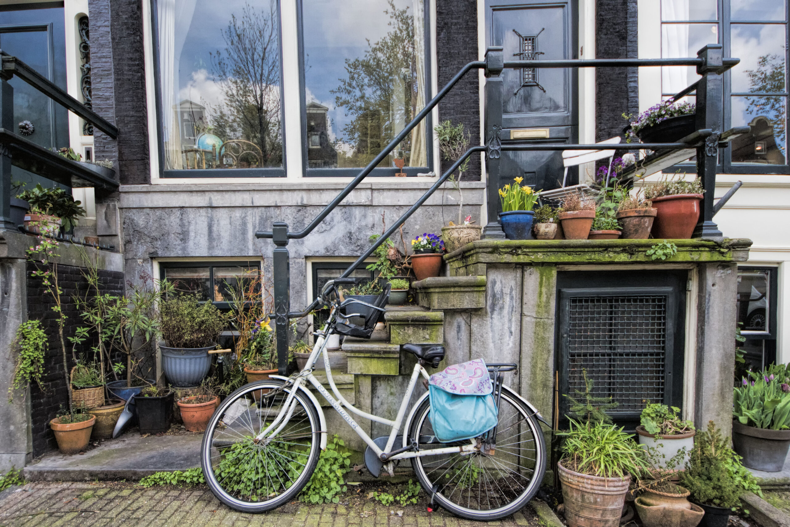 Grachtenpand met witte opoefiets en fleurige bloempotten aan de Leidsegracht in Amsterdam, Nederland