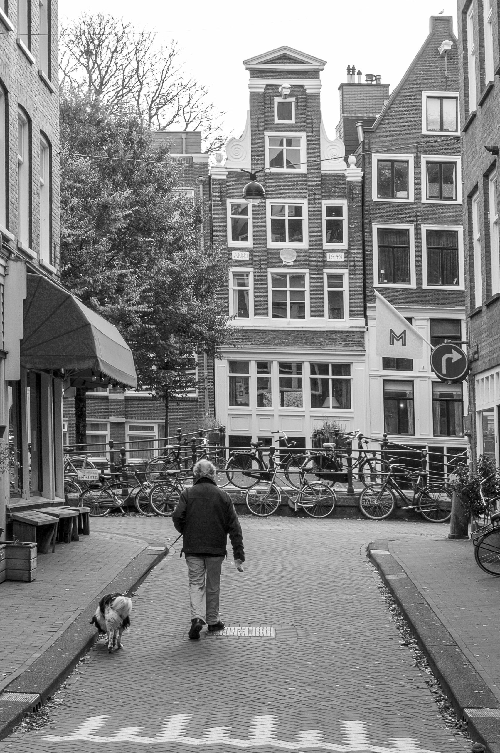 Klassieke zwart-wit straatfotografie van een man die zijn hond uitlaat in de Eerste Laurierdwarsstraat in de Jordaan Amsterdam.