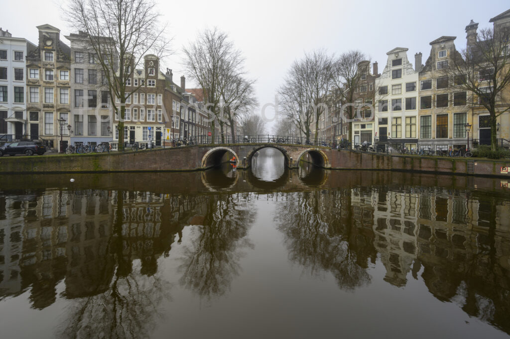Misty morning atmosphere along the Herengracht with historic canal houses and reflections.