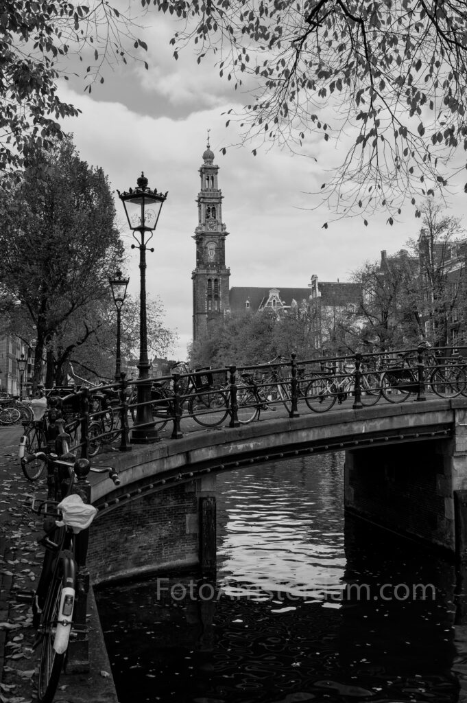 Zwart-wit foto van de Prinsengracht met fietsen, brug en Westerkerk in Amsterdam