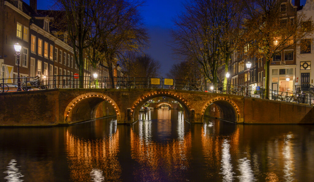 Herengracht in Amsterdam bij avondlicht met verlichte boogbruggen en reflecties in het water
