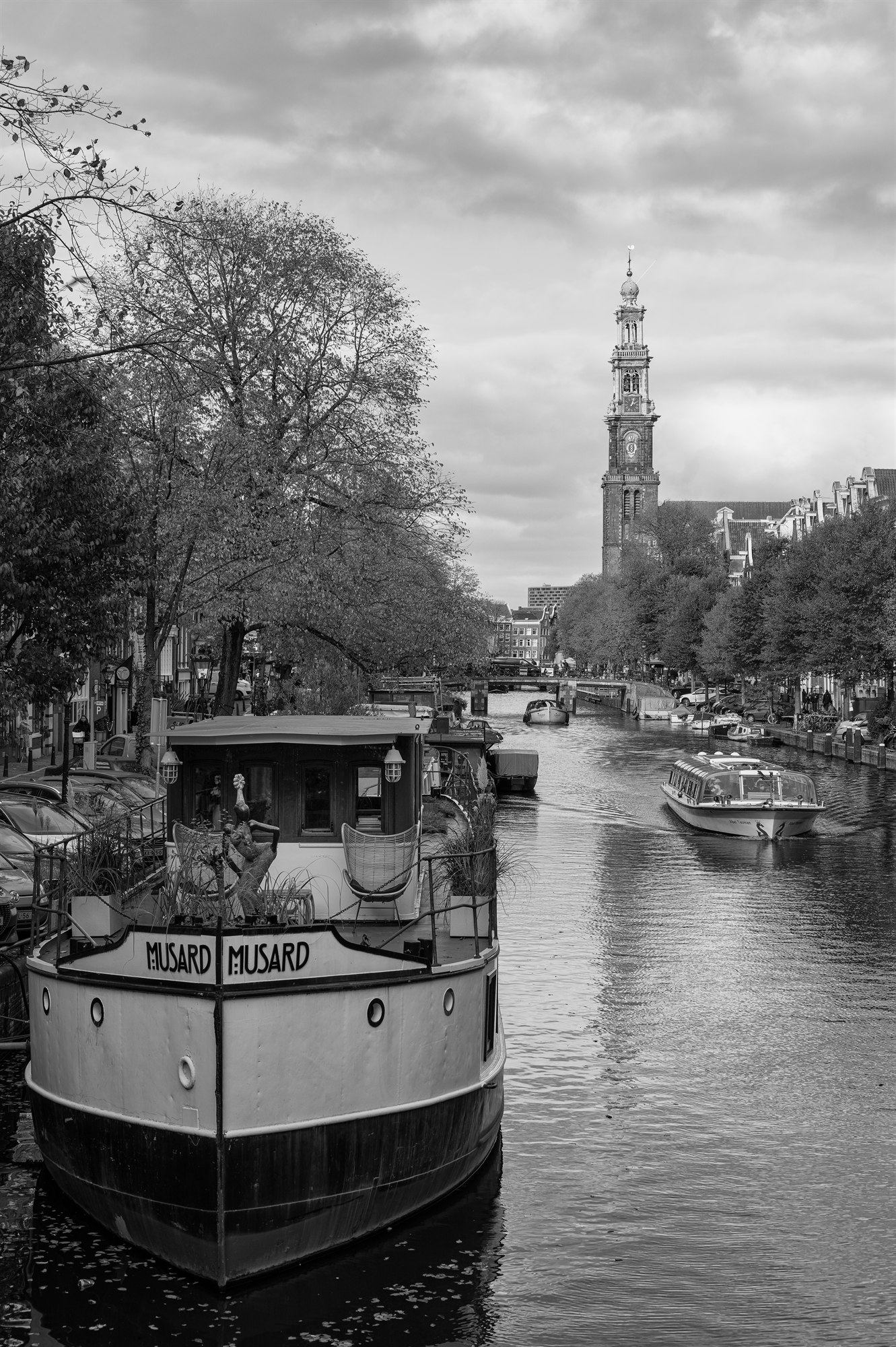 Zwart-wit foto van een rondvaartboot op de Prinsengracht met de Westerkerk op de achtergrond in Amsterdam.